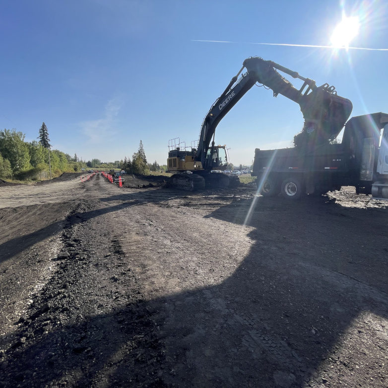 Construction worker overseeing a trench with an excavator in the background