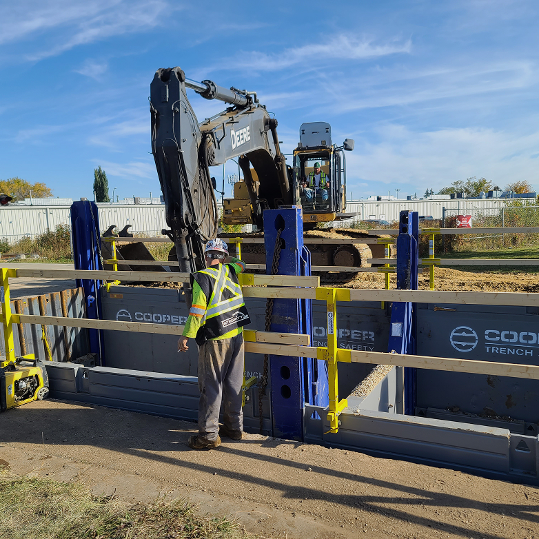 Construction worker overseeing a trench with an excavator in the background
