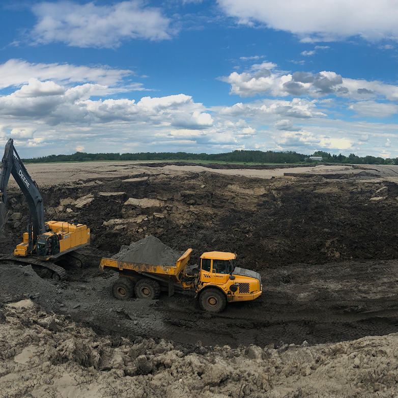 Construction worker overseeing a trench with an excavator in the background