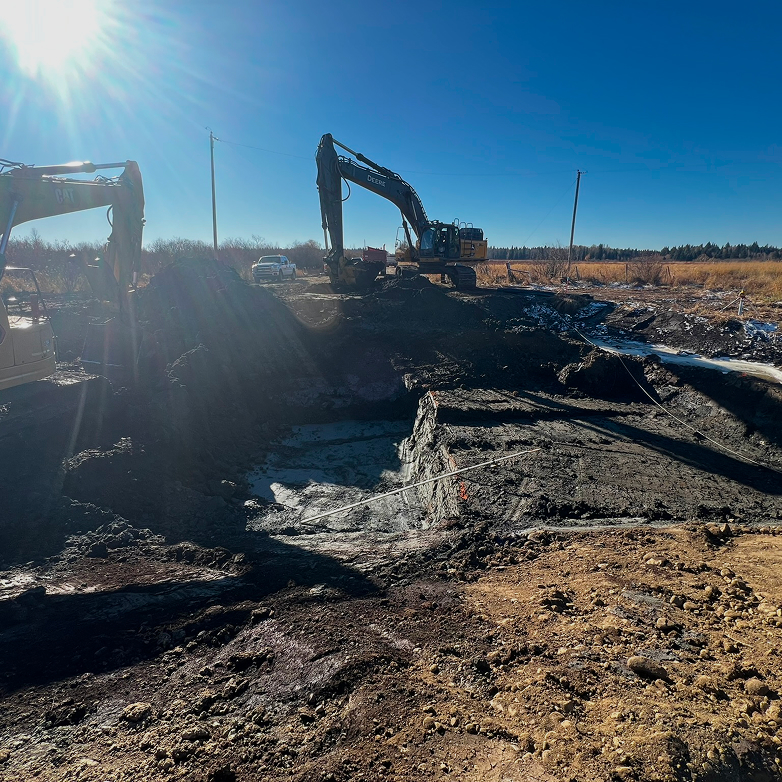 Construction worker overseeing a trench with an excavator in the background